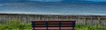 A seafront image with an empty bench facing towards the Burren in Co. Clare.